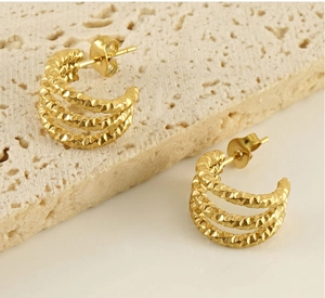 Detailed macro shot of textured gold U-shape earrings on a travertine stone background