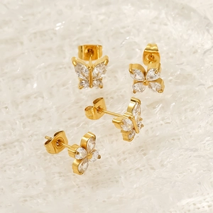 Golden butterfly stud earrings with sparkling cubic zirconia on a textured white background