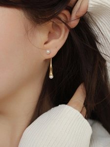 Detailed view of elegant drop earrings featuring white pearls and gold metal on a model