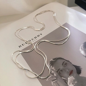 Flat lay of double-layered silver snake chain necklace on a white fashion magazine page