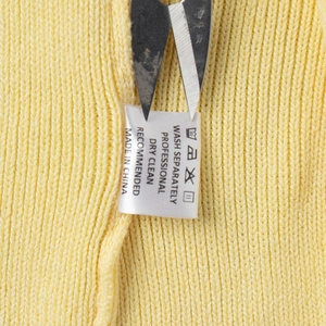 Macro shot of product care label sewn on yellow knit fabric showing washing instructions