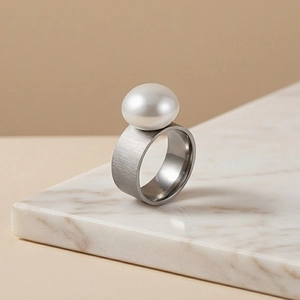 Detail of wide brushed stainless steel ring featuring a large white lustrous pearl