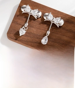 Detailed view of silver bow-shaped cartilage stud with dangling heart-shaped zircons