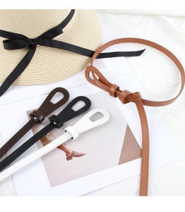 Detail of four colorful slim leather belts for dresses shown with a straw hat on white fabric