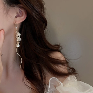 Détail des boucles d'oreilles muguet élégantes avec de longs glands et perles sur modèle