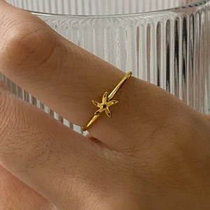 Close-up of a gold star-shaped stainless steel ring worn on a hand near a glass