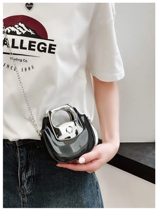 Detail of a shiny black mini crossbody bag with silver metal handle and chain strap