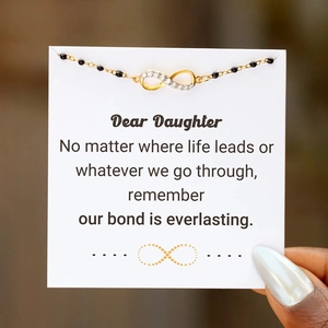 Close-up of golden infinity charm bracelet with black beads on a meaningful message card
