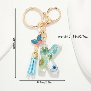 Detail view of resin letter K keychain with dried flowers, blue tassel and butterfly hook