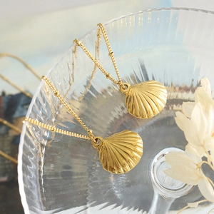 Elegant gold scallop shell pendant necklace with beaded chain on textured glass