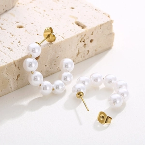 Detail of C-shaped gold hoop earrings with white pearls and zircons on a white background