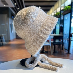 Dettaglio del berretto in peluche beige con orecchie da orso, texture morbida e cinturini