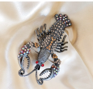 Close-up of a lobster brooch featuring champagne and purple rhinestones on dark metal