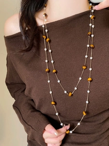 Macro detail of elegant double-layered pearl and tiger eye stone necklace on a model