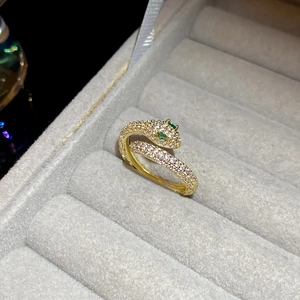 Close-up of gold-plated snake ring with white crystals and green emerald-like eyes