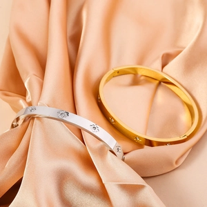 Detailed view of gold and silver stainless steel bangles with floral motifs on satin