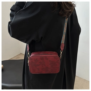 Detail view of red embossed leather square bag with colorful jacquard wide shoulder strap
