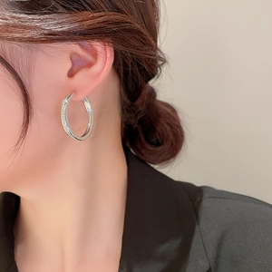 Close-up of silver geometric hoop earring with sparkling rhinestones on model's ear