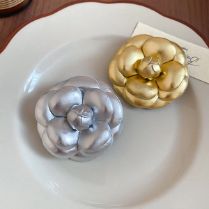 Macro shot of gold and silver metallic camellia pins displayed on a ceramic dish