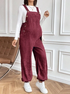Detail of adjustable waist and side buttons on burgundy corduroy maternity overalls