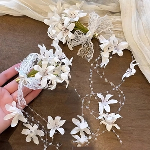 Detail of white fabric floral hair clip with lace bow, pearl heart and long tassels
