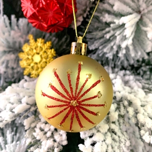 Close-up of golden Christmas ball with red glitter star pattern on snowy pine branch