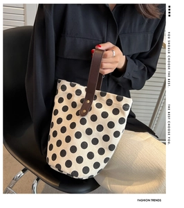 Close-up of canvas bucket bag featuring bold black polka dots and brown leather handles