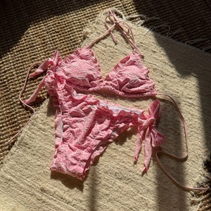 Close-up of pink bikini featuring floral embroidery and delicate ruffle edges on a rug