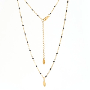 Close-up of gold stainless steel feather pendant necklace with black seed beads detail