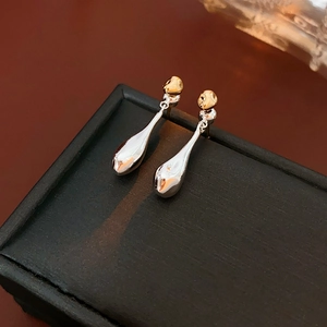 Detail of gold ball stud and silver teardrop pendant on black textured jewelry box