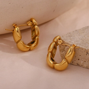 Detailed view of chunky 18K gold plated hoop earrings on textured stone and fabric
