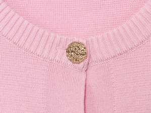 Dettaglio dello scollo in maglia rosa con elegante bottone dorato con trama a spirale