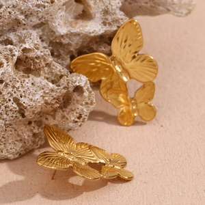 Macro shot of 18K gold-plated stainless steel double butterfly earrings on a stone