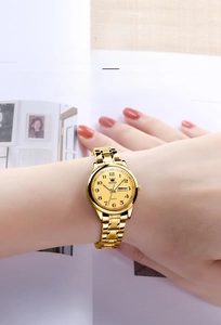 Close-up of OLEVS gold quartz watch with crystal bezel and date display on a wrist