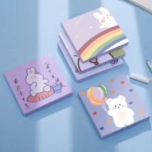 Close-up of cute cartoon alpaca and rabbit memo pads on a blue desk with office pens