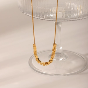 Vue détaillée du collier à billes dorées avec pendentif carré minimaliste sur verre