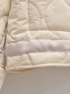 Detail of cream white quilted jacket featuring curved stitching and woven hem border