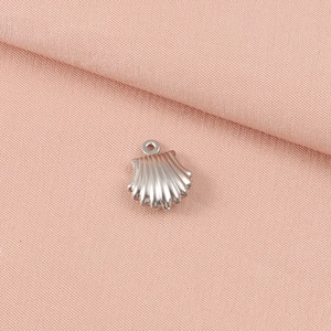 Detail view of a silver seashell pendant charm on soft pink fabric background