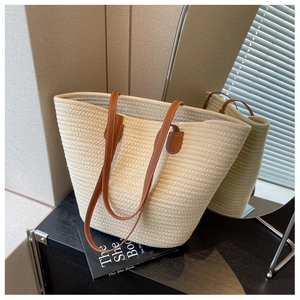Close-up of woven cotton tote bag with brown faux leather handles in a cozy indoor setting