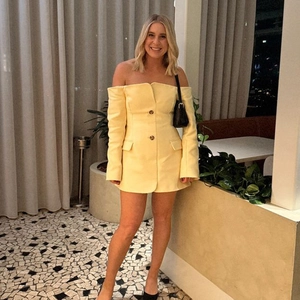 Detail of yellow off-the-shoulder blazer dress featuring long sleeves and button accents