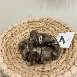 Detailed view of a brown plaid scrunchie with a brand label on a woven straw mat