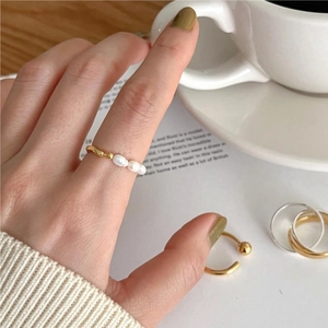 Close-up of gold pearl ring featuring three white pearls worn in a lifestyle setting
