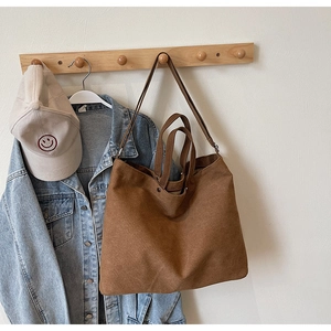 Brown canvas tote bag hanging on wooden hook with casual denim jacket and cap