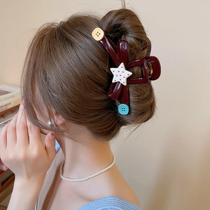 Detail of red acrylic hair claw with star and button motifs on hair style