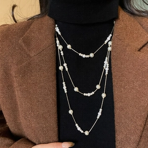 Close-up of triple-layered pearl necklace with crystal pave beads on dark knitwear