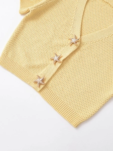 Detail of star-shaped gold buttons on pale yellow knit cardigan with waffle texture