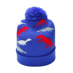 Close-up of blue knitted beanie featuring colorful dinosaur jacquard and a fluffy pom-pom