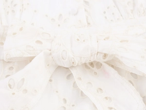 Detailed macro view of white cotton eyelet lace fabric with a decorative bow embellishment