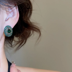 Side view of a vintage oval earring with green gems and crystals on a model's ear