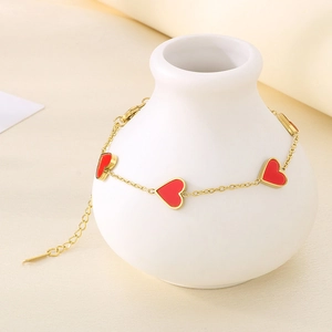 Detail of a gold titanium bracelet with red enamel hearts on a white ceramic vase